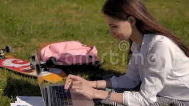 一个年轻学生在公园草地上躺着时使用她的笔记本电脑的侧视图